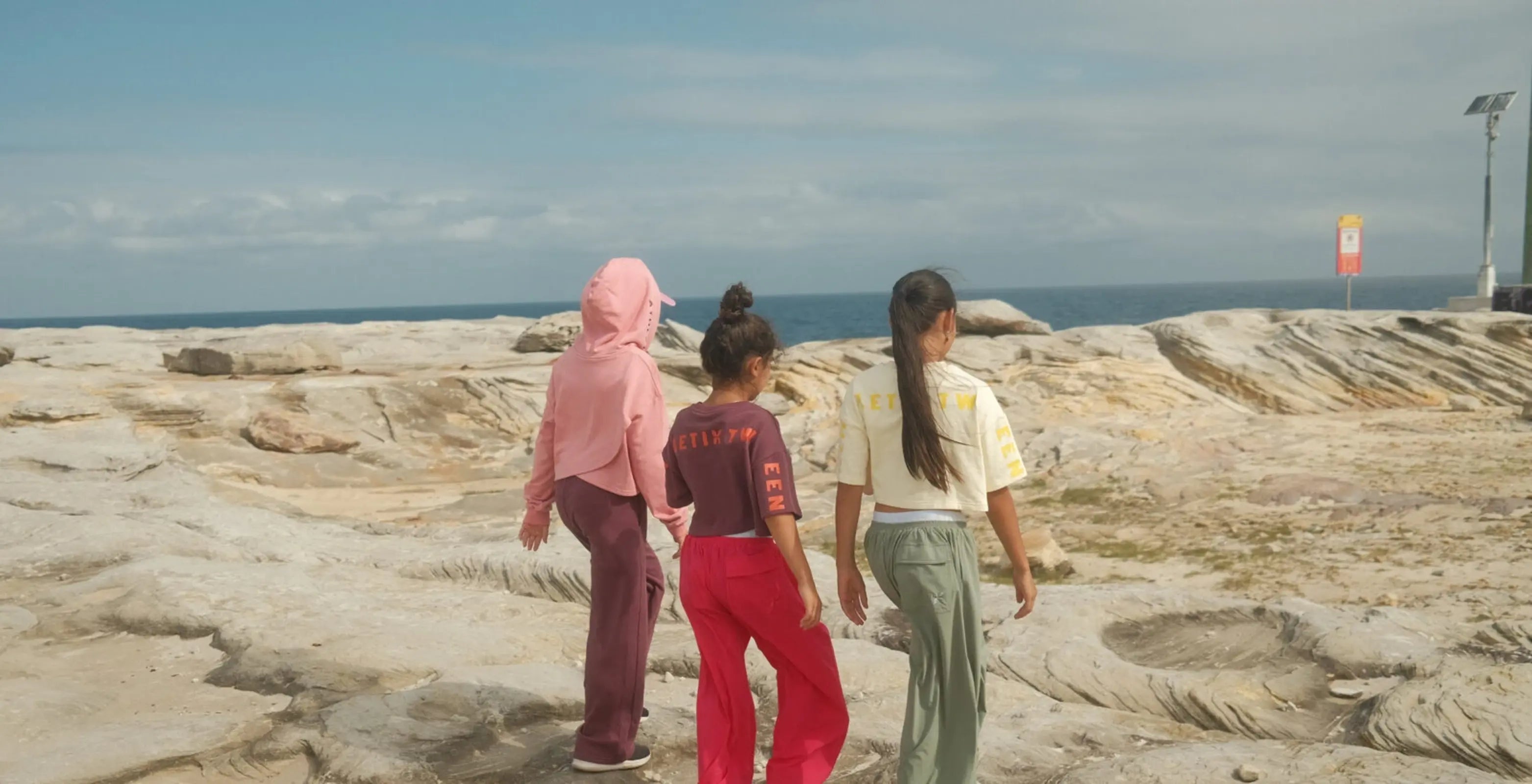 Three people walking on a rocky coastal landscape with ocean in the background