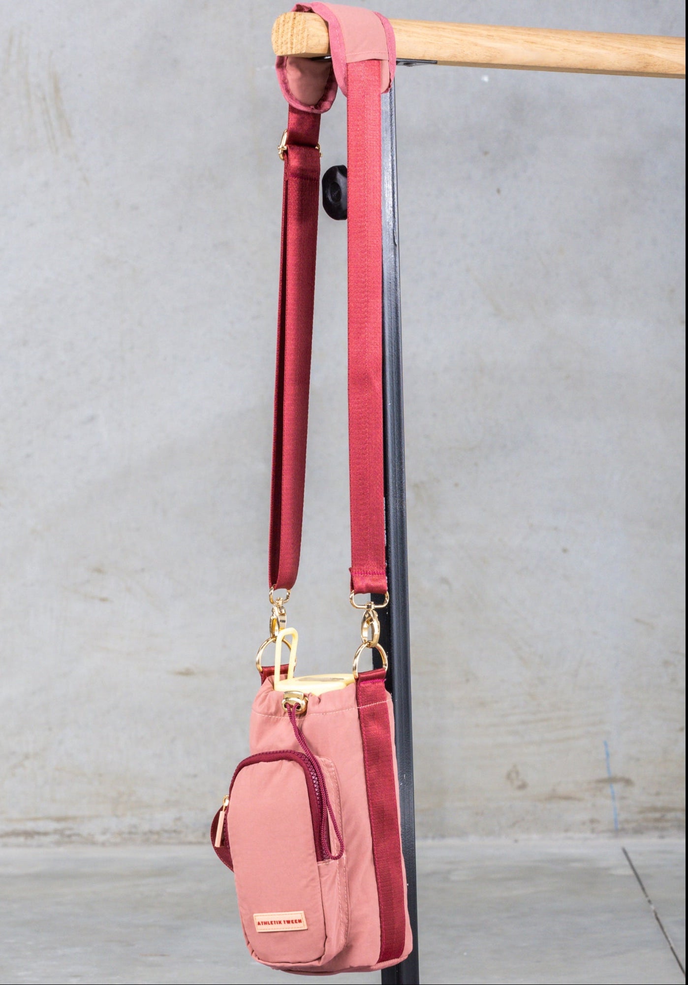 Pink crossbody bag with red strap hanging on a wooden rod against a gray wall.